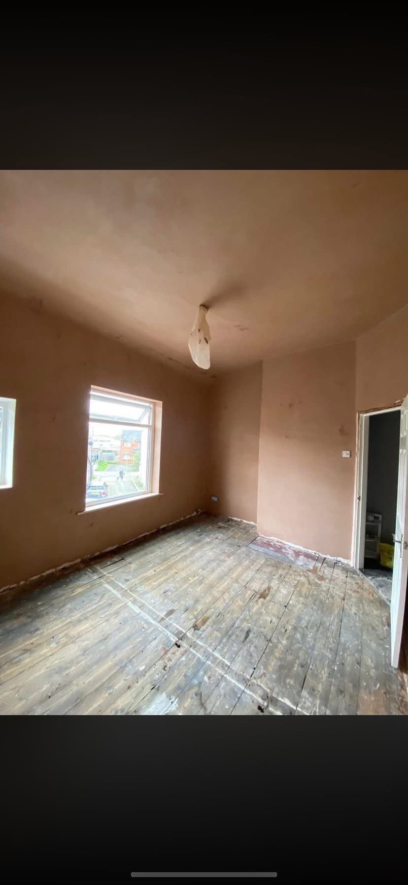 A freshly plastered room with a smooth, flat finish and bare floorboards
