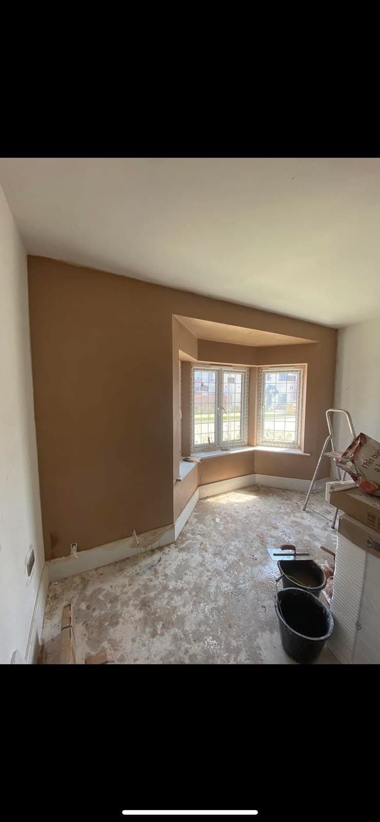 A finished bay window room, skimmed and ready, with a ladder and buckets still out